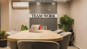 Een vergaderruimte met een grote tafel, grijze stoelen, een laptop, boeken en een bord waarop 'TEAM WORK' staat.