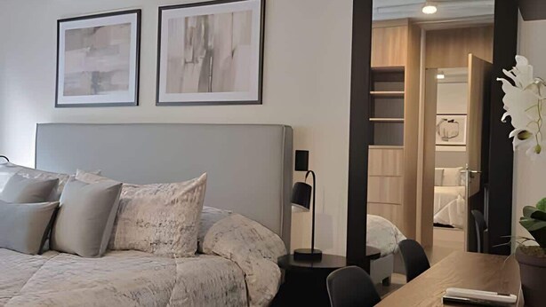 Een moderne slaapkamer met een groot bed, nachtkastje, bureau en stoel. Twee ingekaderde foto’s hangen aan de muur.
