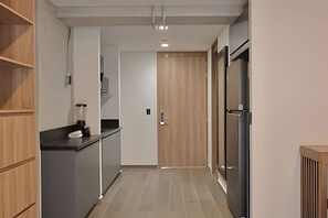 Ein schmales Entree mit einer Küchenzeile an einer Seite, inklusive Kühlschrank, Mikrowelle und einer Arbeitsfläche.