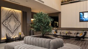 A modern living area with a sectional sofa, a potted plant, and a flat-screen TV mounted on the wall. - Cozy 1-bedroom apartment in beautiful Riyadh with AC and gym access (Riyadh)