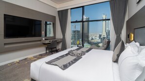 A hotel room with a large bed, a desk, a TV, and a view of the cityscape. - Cozy 1-bedroom apartment in beautiful Riyadh with AC and gym access (Riyadh)