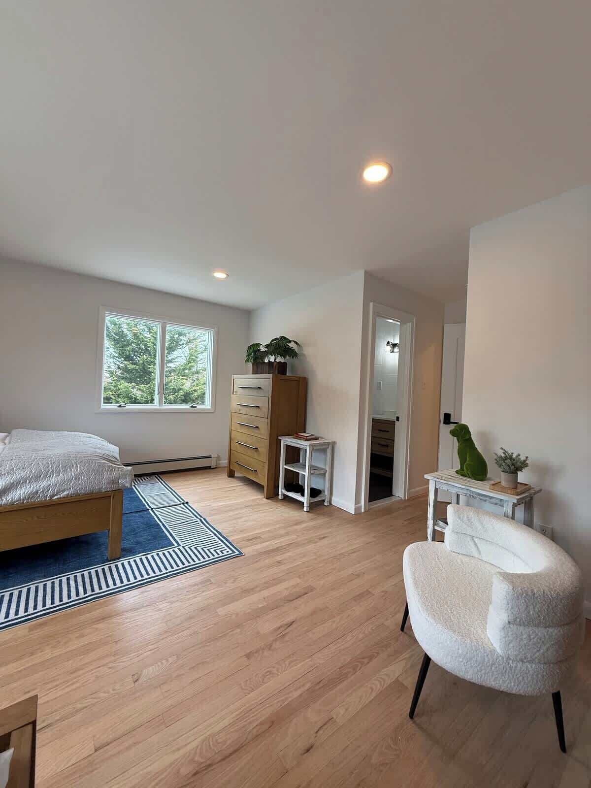 A bedroom with a bed, dresser, chair, and a small table with plants.