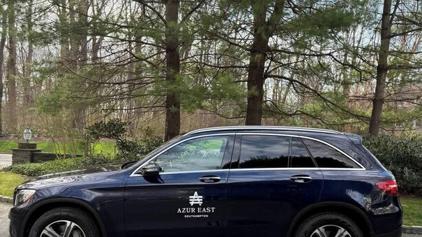 Ein dunkelblauer SUV steht auf einem gepflasterten Platz, Bäume sind im Hintergrund zu sehen.