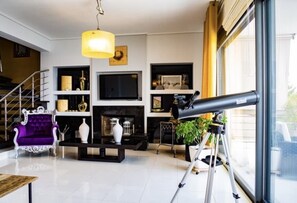 Un salon moderne avec une cheminée, un télescope fixé au mur et un fauteuil violet.