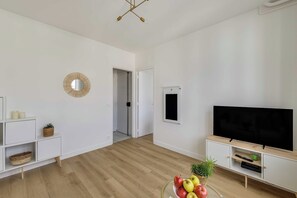 Ein modernes Wohnzimmer mit Flachbildfernseher, Holzboden, weißen Wänden und minimalistischer Einrichtung.