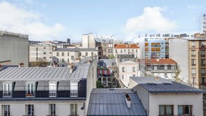 A cityscape with various buildings, including a prominent building with a sloped roof and multiple windows. - Cozy Apartment 1b/2p - Paris 14th (Paris)