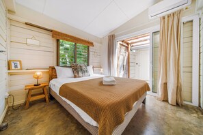 Ein Schlafzimmer mit Bett, Nachttisch, Lampe und einem Fenster mit Vorhängen.