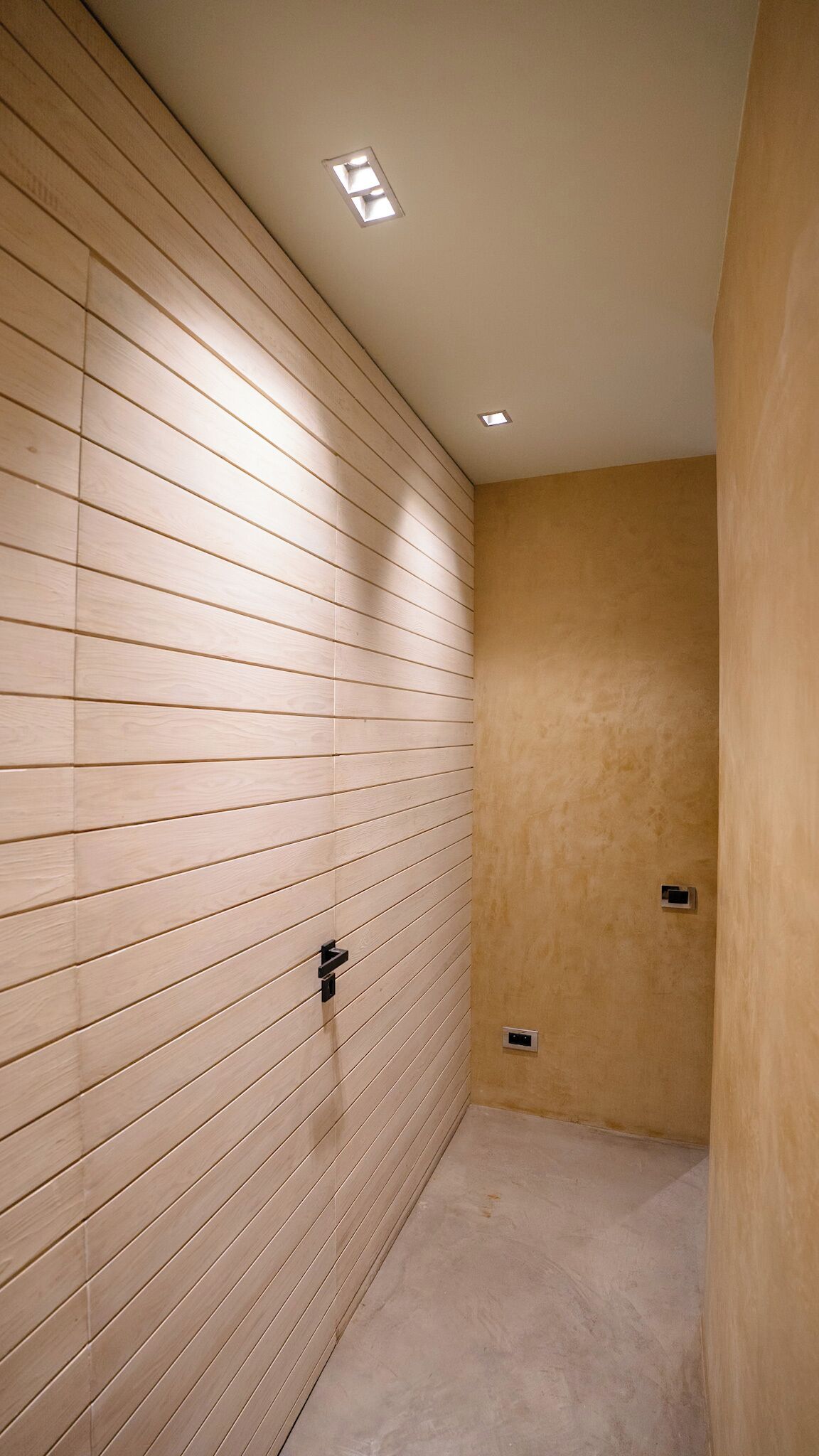 Un couloir étroit, avec un mur recouvert de lambris en bois et un autre mur uni, ainsi qu’un luminaire au plafond.