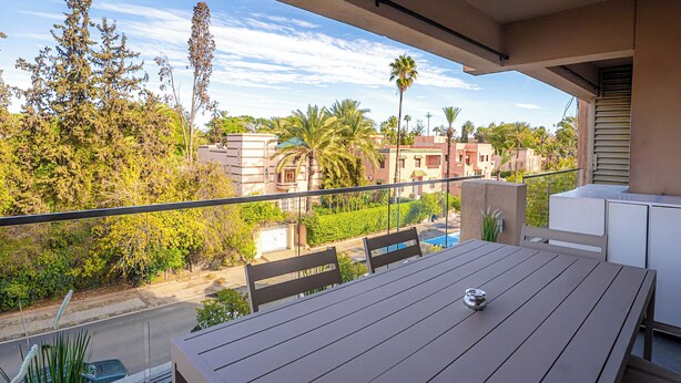 Een balkon met een tafel en stoelen, met uitzicht op een woonwijk met palmbomen en gebouwen.