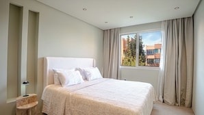 Een slaapkamer met een bed, nachtkastje, lamp en een raam met gordijnen.