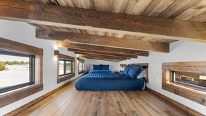 Quarto com uma cama grande, vigas de madeira e janelas.