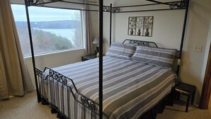 A four-poster bed with a view of a lake through a window, a nightstand, and a wall-mounted artwork. - 4-bedroom house overlooking Lake Norfork with AC comfort (Mountain Home)