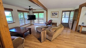 A spacious living room with a wooden floor, a television, a sofa, and a chair. - 4-bedroom house overlooking Lake Norfork with AC comfort (Mountain Home)