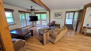 A spacious living room with a wooden floor, a television, a sofa, and a chair. - 4-bedroom house overlooking Lake Norfork with AC comfort (Mountain Home)