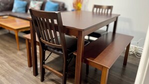 Un coin repas avec une table et des chaises en bois, un banc et un canapé agrémenté de coussins à l’arrière-plan.