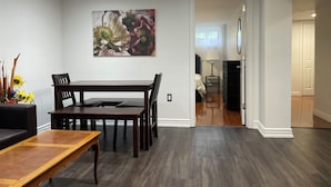 Un coin repas avec une table et des chaises en bois, un tableau accroché au mur et un couloir menant à une chambre.