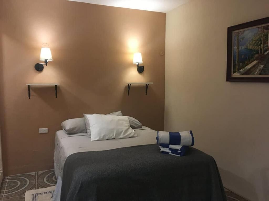 Habitación de hotel con cama, dos lámparas de pared, un cuadro y una mesita.