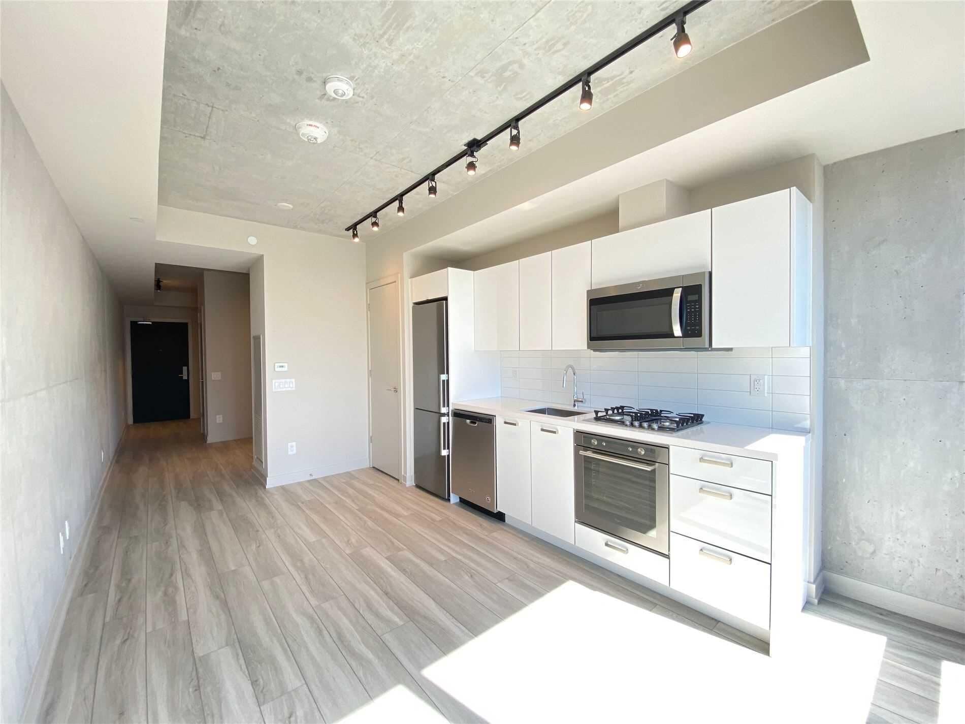 A modern kitchen with white cabinets, a stainless steel refrigerator, a microwave, and a gas stove.