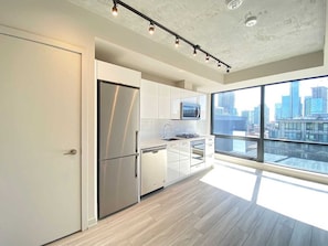 A modern kitchen with stainless steel appliances, white cabinetry, and a large window offering a city view.