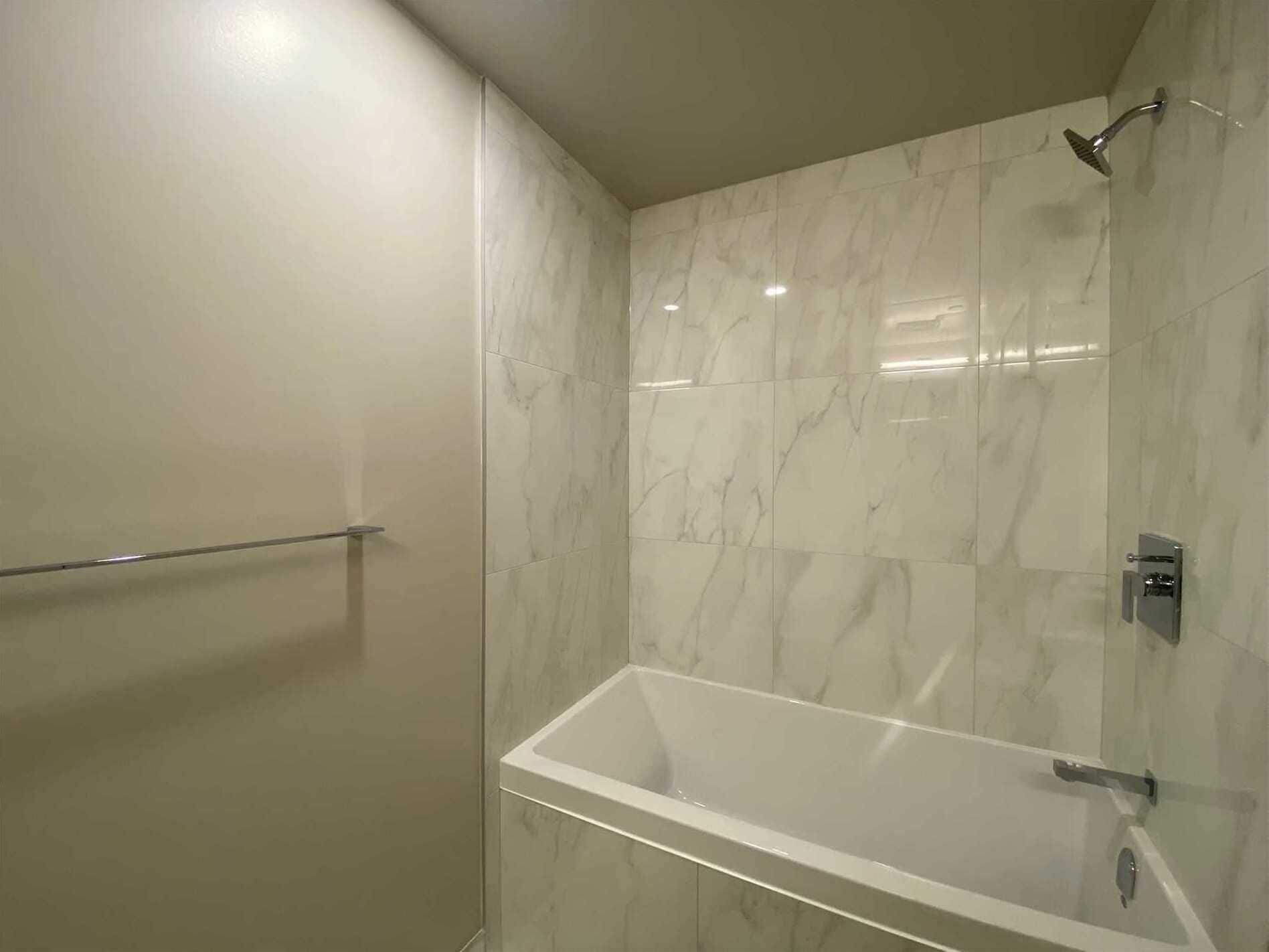A modern bathroom with a glass-enclosed shower, a white bathtub, and a marble wall.