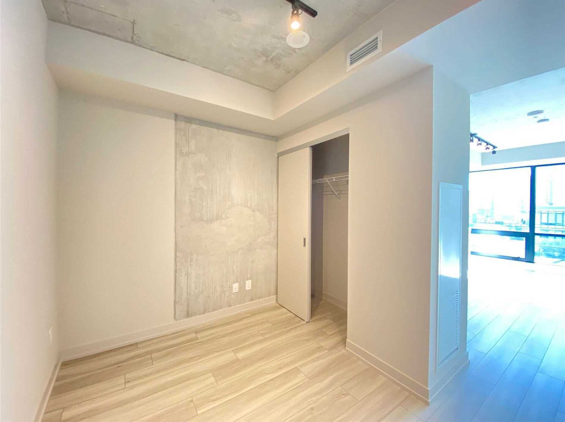 A room with a wooden floor, a closet, and a large window with a view of the outside.