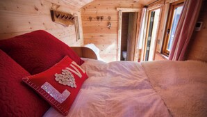 Interior de una cabaña de madera con una cama, una pared de madera decorada con un corazón y una ventana.