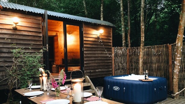Una cabaña de madera con un jacuzzi, una mesa de comedor para dos personas y un farol.