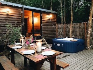 A wooden cabin with a hot tub, a dining table set for two, and a lantern.