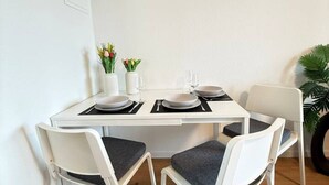 A white dining table with four chairs, each with a dark cushion. There are two vases with flowers on the table. - Lake view apartment with balcony (Rorschach)