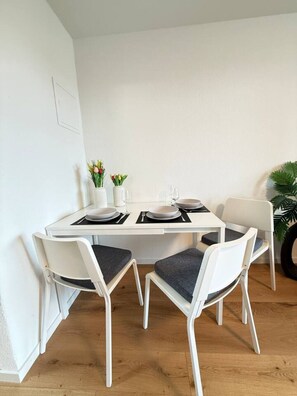 A white dining table with four chairs, each with a dark cushion. There are two vases with flowers on the table.