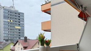 A balcony with a wooden table and chairs, a potted plant, and a view of buildings. - Lake view apartment with balcony (Rorschach)