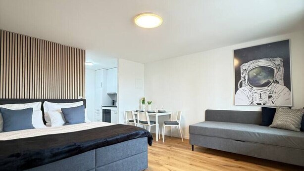 A modern room with a bed, a sofa, a dining table, and a wall-mounted artwork. - Lake view apartment with balcony (Rorschach)