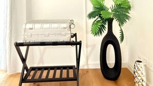 A flat-screen TV mounted on a wall, a metal rack with a suitcase, a potted plant, and a decorative vase on the floor. - Lake view apartment with balcony (Rorschach)