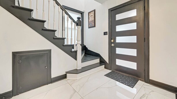 Una escalera con balaustres blancos, una puerta oscura con paneles de vidrio esmerilado y un piso de mármol.