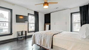 Un dormitorio con cama, ventilador de techo, televisión y ventana con cortinas.