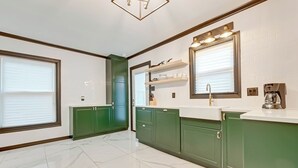 Una cocina moderna con armarios verdes, encimeras blancas y suelo de mármol.
