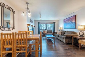 A living room with a wooden dining table, chairs, a sofa, a coffee table, and a painting on the wall.