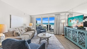 Een moderne woonkamer met een bank, fauteuils, een salontafel, een televisie en uitzicht op het strand.
