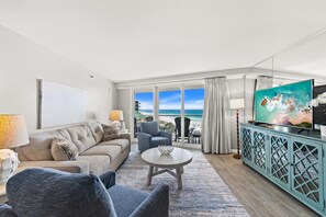 A modern living room with a sofa, armchairs, a coffee table, a TV, and a view of the beach. - Beachfront Balcony ~ Pool (Miramar Beach)