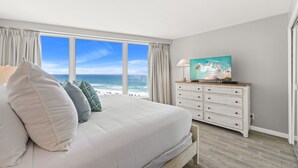 Een slaapkamer met een groot bed, een dressoir, een schilderij en uitzicht op de oceaan.