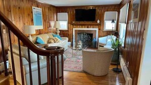 A wooden-paneled living room with a fireplace, a sofa, a coffee table, and a TV mounted on the wall. - Immaculate 3 bedrooms and very private backyard with firepit. (Bloomfield)
