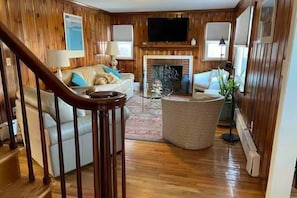 A wooden-paneled living room with a fireplace, a sofa, a coffee table, and a TV mounted on the wall.