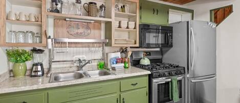 A kitchen with green cabinets, a stainless steel refrigerator, a stove, and a microwave.