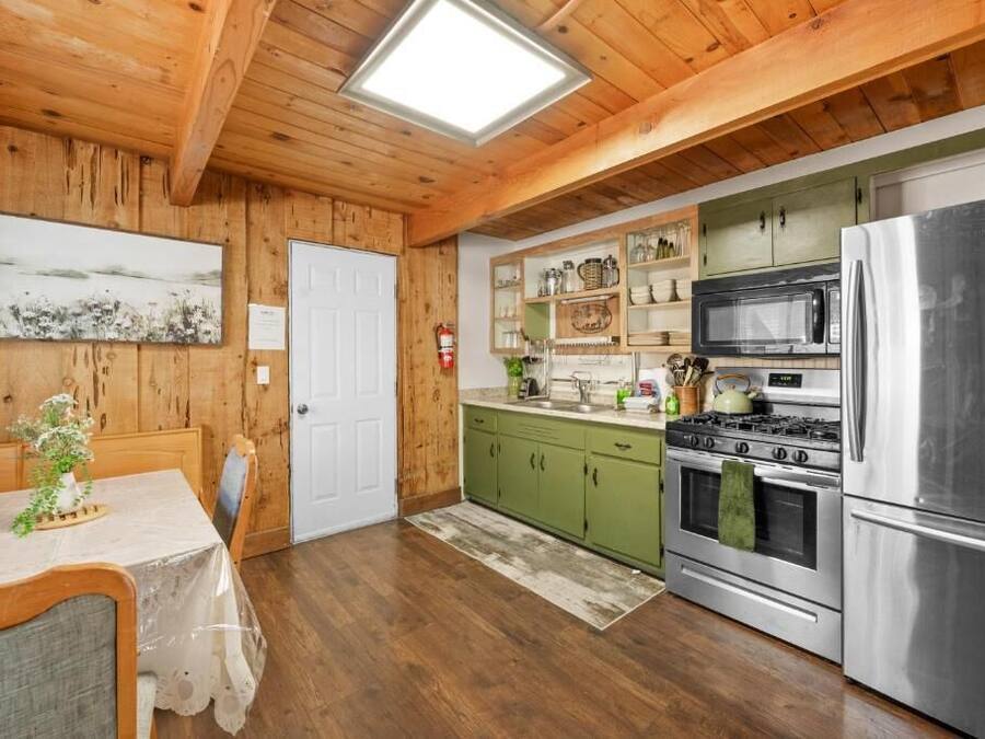 A wooden interior with a dining table, kitchen with green cabinets, stainless steel appliances, and a skylight.