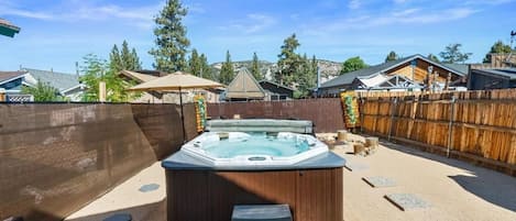 A backyard with a hot tub, a wooden deck, and a wooden fence.