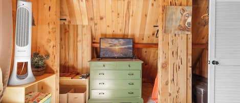 Habitación con paredes de madera, un aparador verde, un televisor y una puerta blanca.