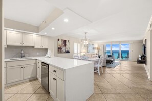 A modern kitchen with a large island, white cabinetry, and a dining area with a view. - Stunning Gulf View and Beach Front Coastal Escape (Miramar Beach)