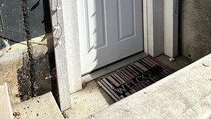 Una porta bianca con una finestra sopra, un gradino in metallo che conduce alla porta e un tappetino d'ingresso con la scritta 'WELCOME'.