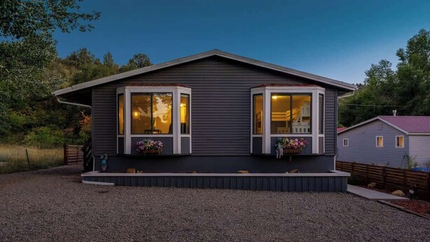 Una casa a due piani con vialetto in ghiaia, un portico con fioriere e una finestra ben visibile.