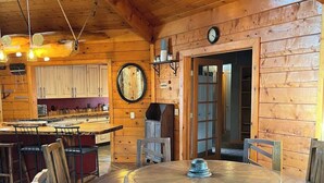 Un intérieur en bois avec une table de salle à manger ronde, des chaises, un coin cuisine et une horloge au mur.